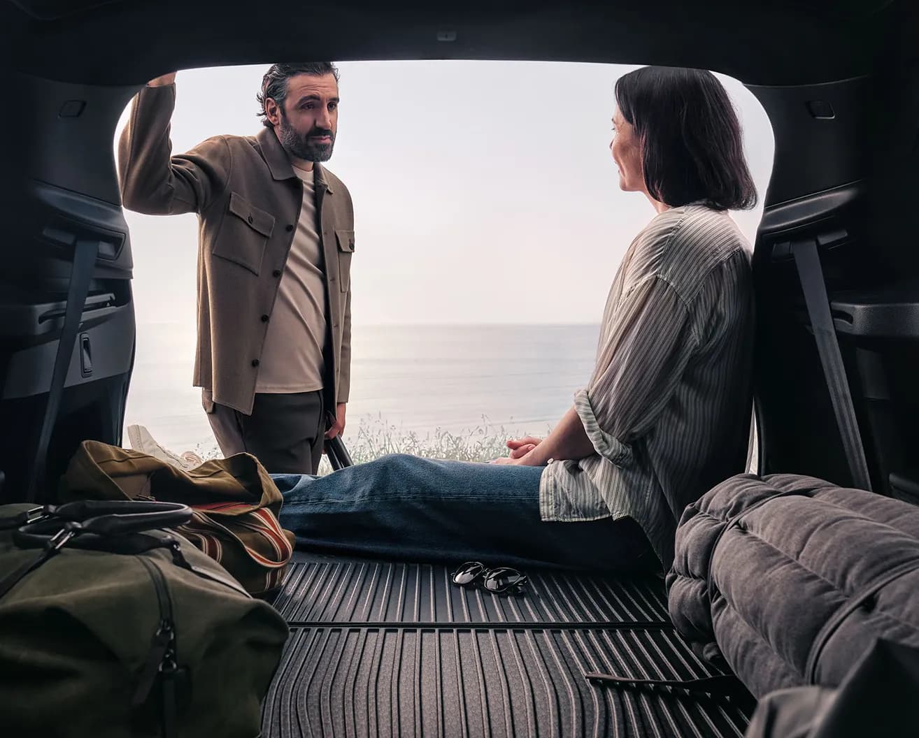 Casal guardando bagagens no porta-malas de um Volvo com vista para o mar